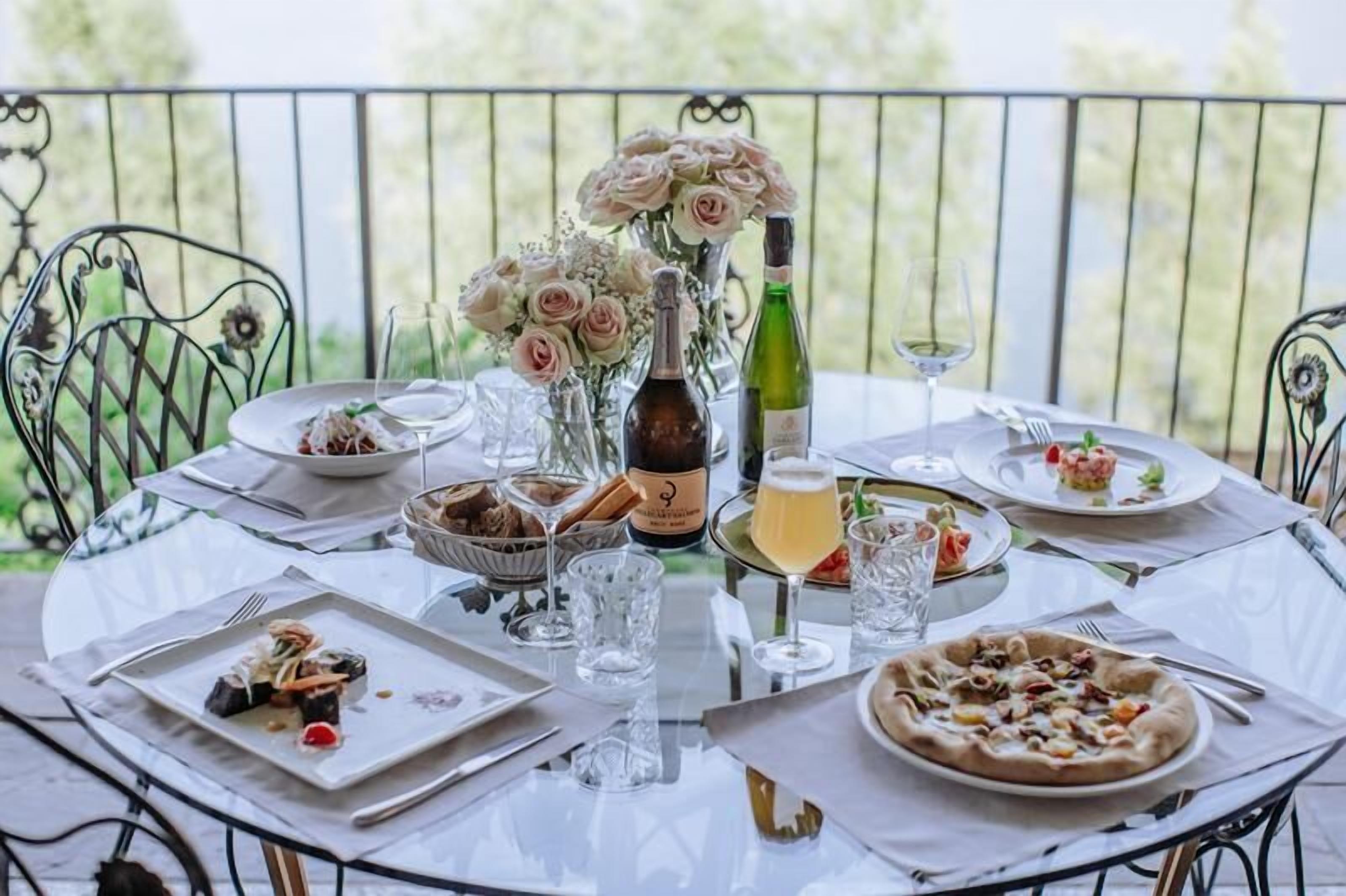 A round dining table set outdoors with various dishes, glasses, and a bottle of wine.