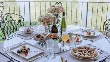 A round dining table set outdoors with various dishes, glasses, and a bottle of wine.