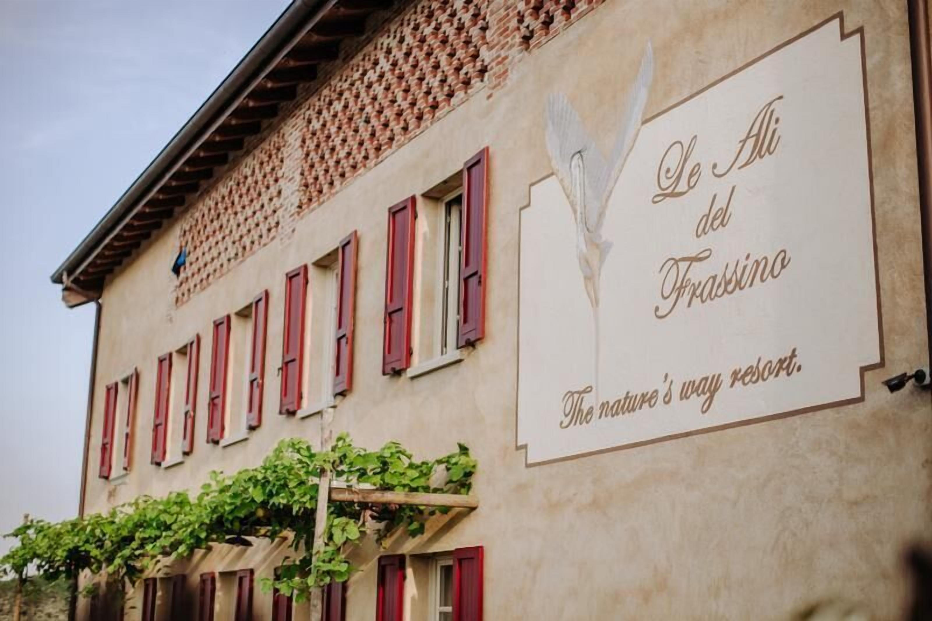 A building with red shutters and a sign that reads "Le Ali del Frassino - The nature's way resort."