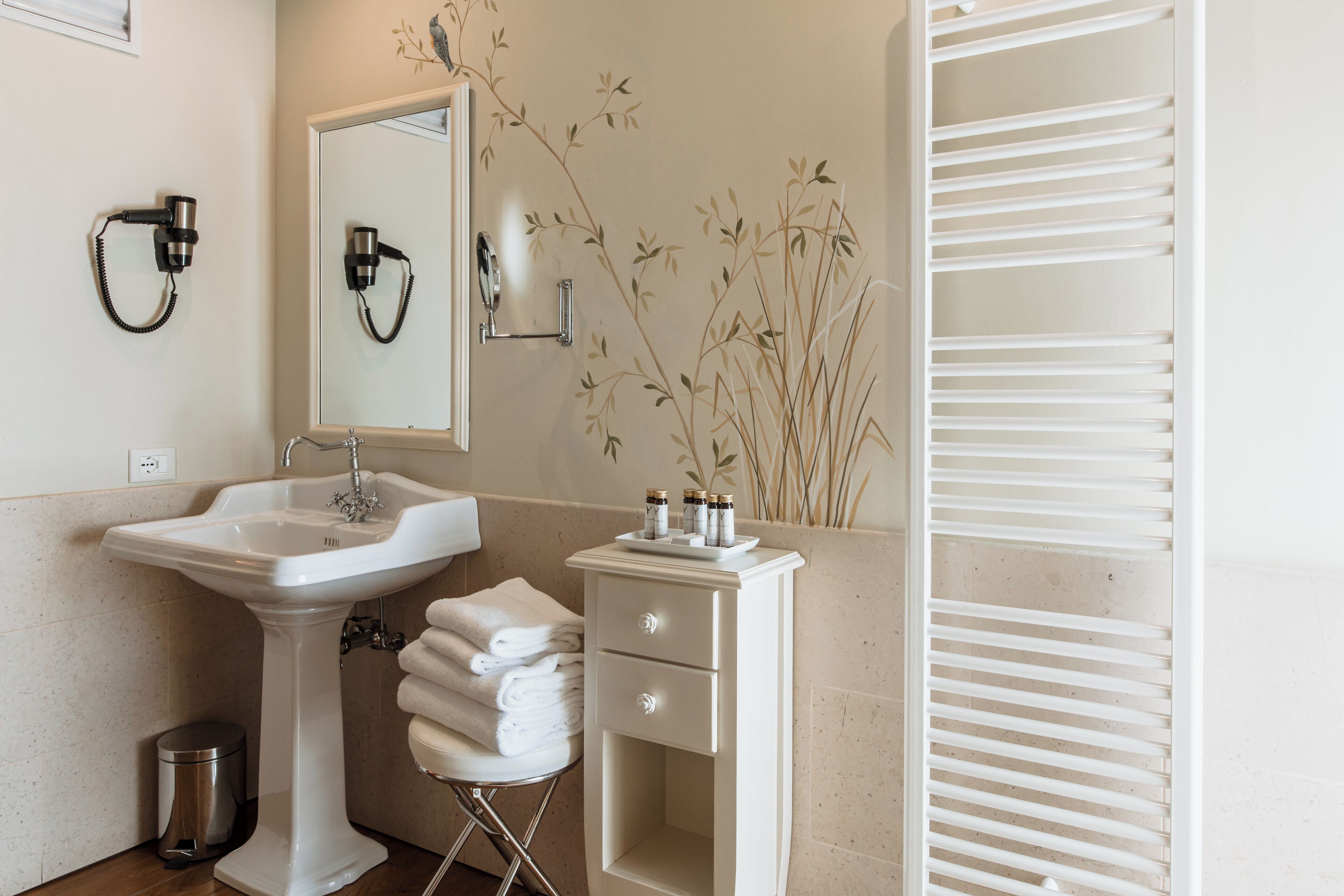 Une salle de bain avec un lavabo sur colonne, un miroir, un porte-serviettes et un petit meuble contenant des articles de toilette.
