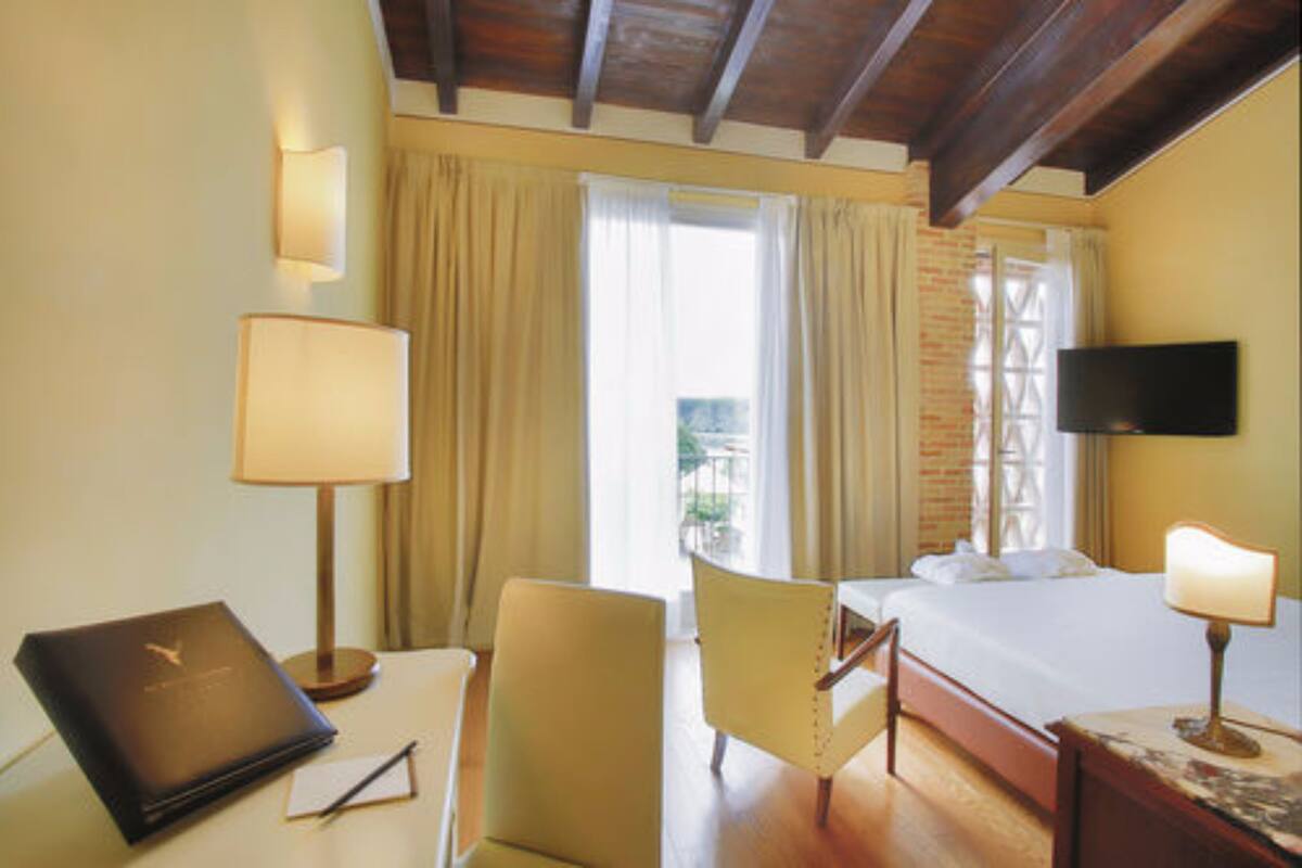 Habitación de hotel con cama, escritorio, silla, televisor y ventana con cortinas.