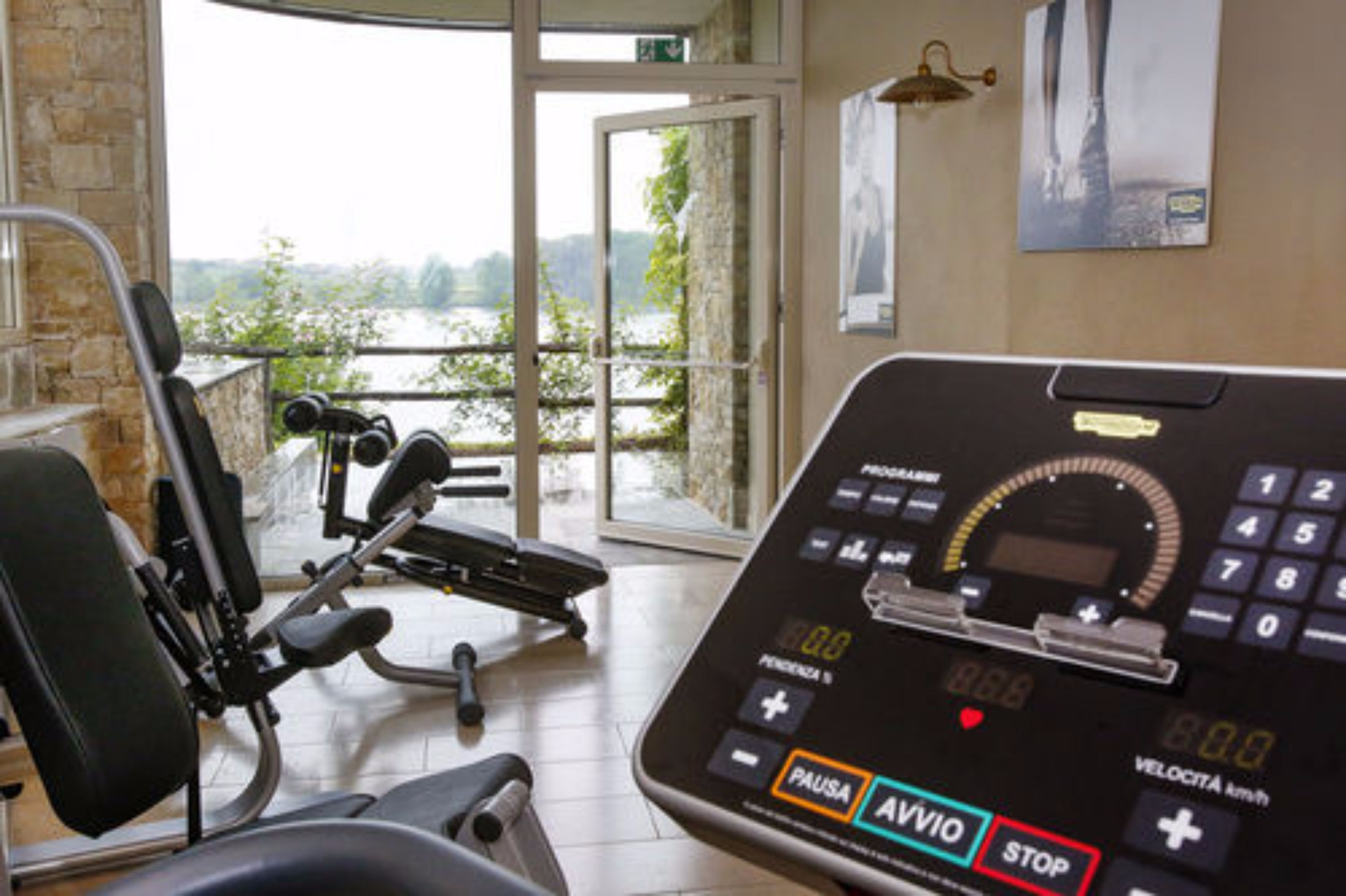 Un gimnasio con equipo de ejercicio, un velocímetro digital y vistas a un lago a través de amplias ventanas.