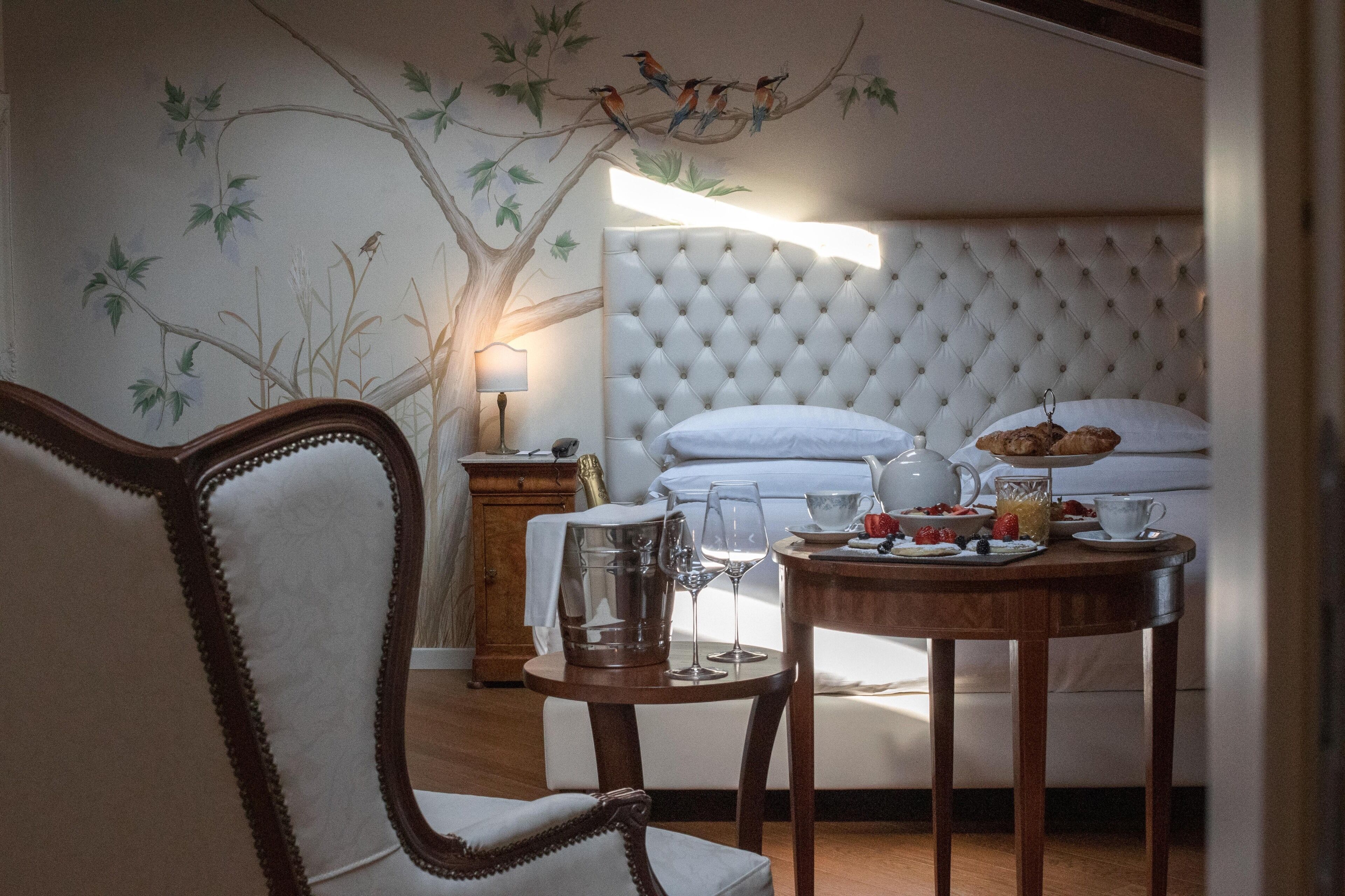 Ein Schlafzimmer mit einer gepolsterten Kopfteile, einem Esstisch mit Frühstücksangeboten, einem Stuhl und einem Nachttisch mit Lampe.