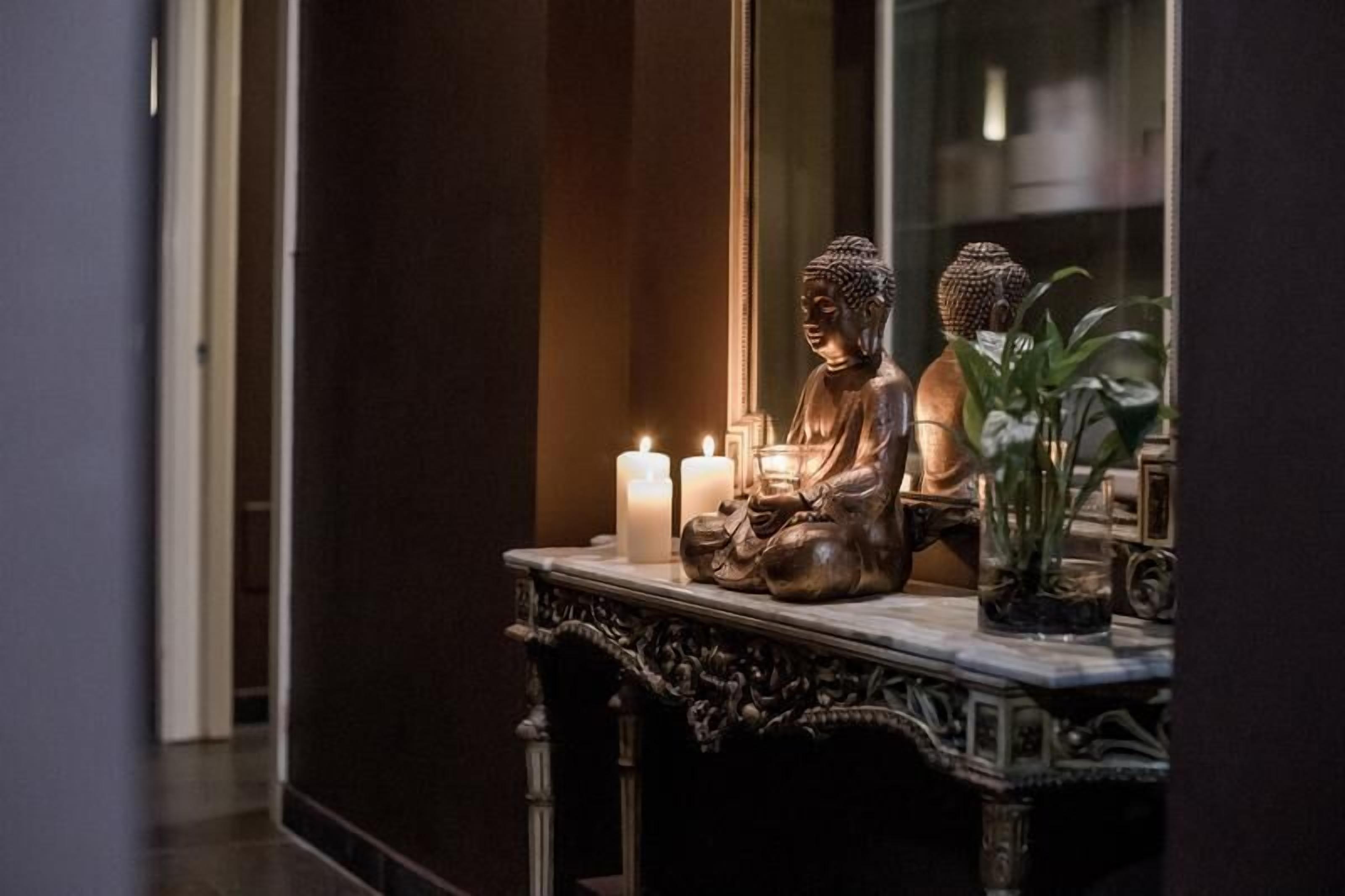 A statue of Buddha on a marble table with candles and a potted plant.