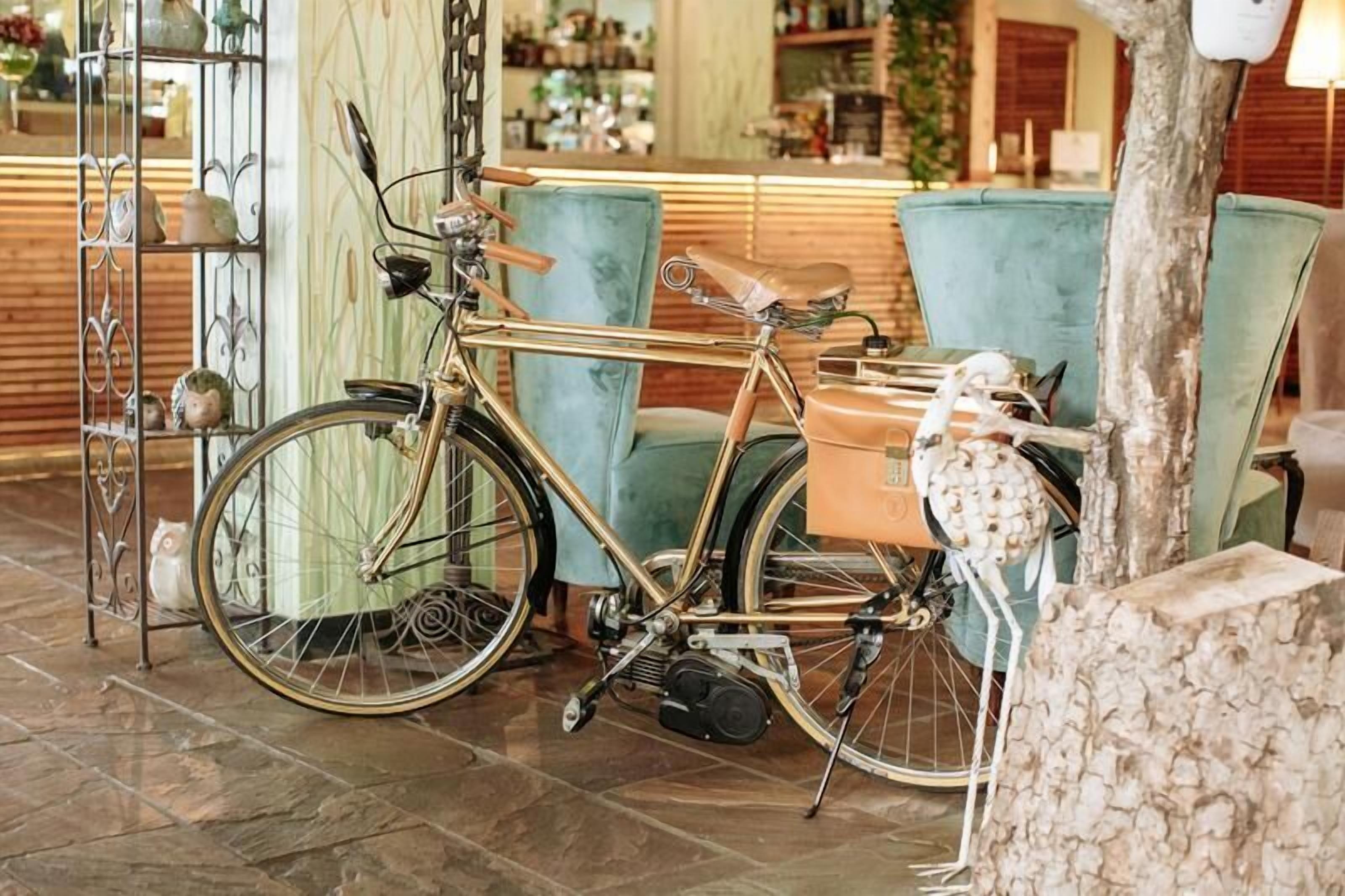 Un vélo d’époque dans un hall d’entrée, avec un fauteuil de couleur turquoise et une sculpture représentant un tronc d’arbre.