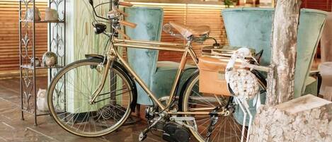 Un vélo d’époque dans un hall d’entrée, avec un fauteuil de couleur turquoise et une sculpture représentant un tronc d’arbre.