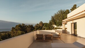 A rooftop terrace with a view of the sea, wooden furniture, and a modern building. - Besai Ibiza Boutique Hotel - New Opening (Sant Josep de sa Talaia)