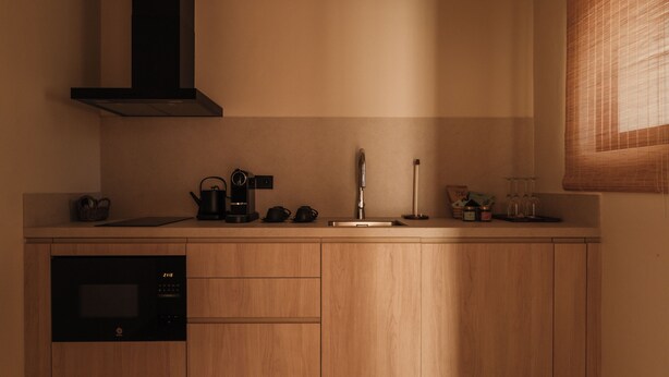 A modern kitchen with wooden cabinets, a black range hood, and a window with blinds. - Besai Ibiza Boutique Hotel - New Opening (Sant Josep de sa Talaia)