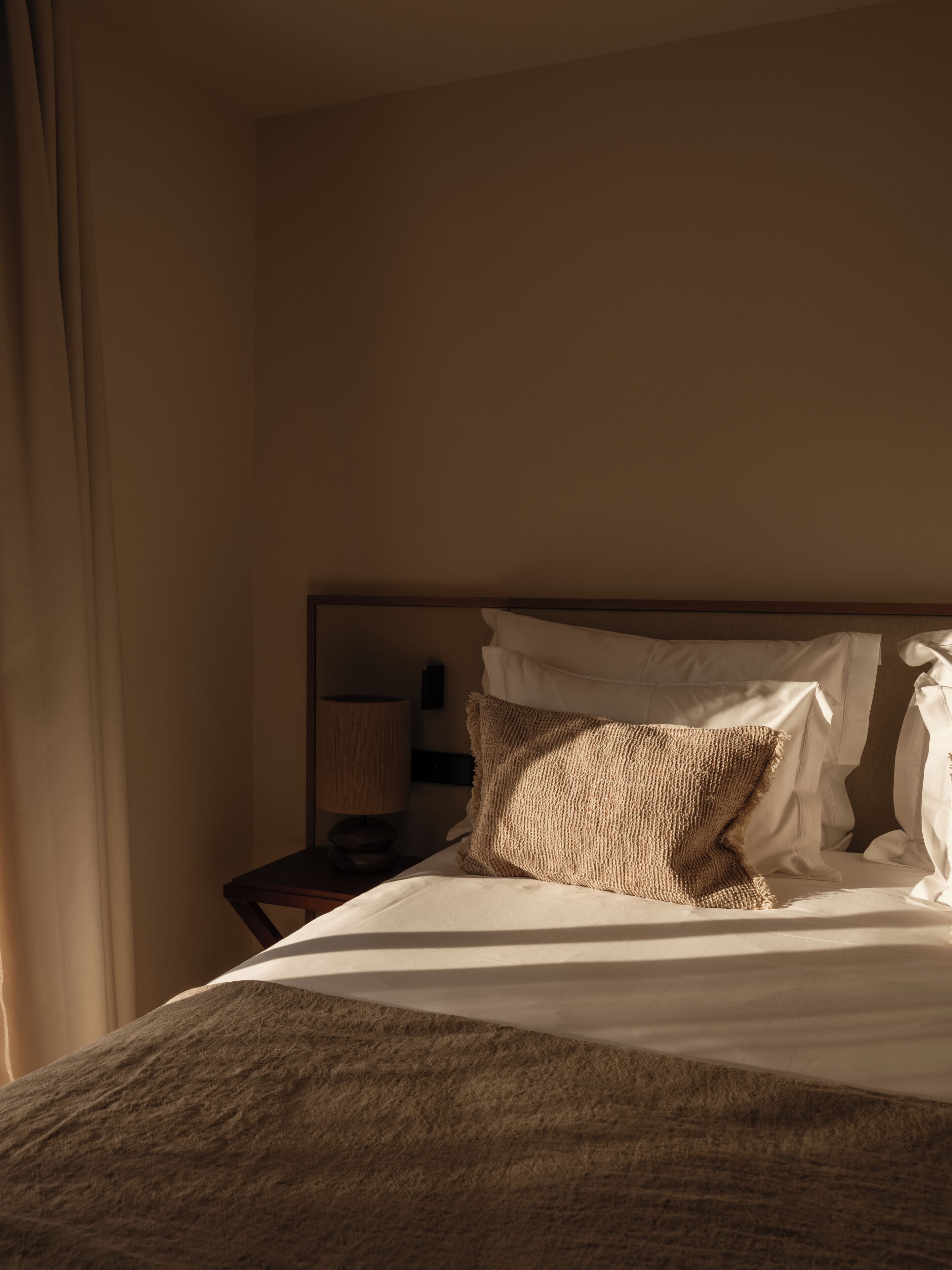 A hotel room with a bed, a nightstand, and a lamp.