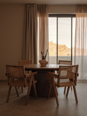 A dining area with a round wooden table, four wicker chairs, and a vase with flowers.