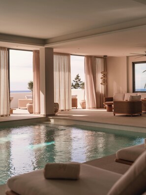 A modern indoor pool area with a view of the sea, large windows, and comfortable seating. - Besai Ibiza Boutique Hotel - New Opening (Sant Josep de sa Talaia)