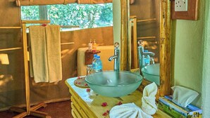A compact, rustic bathroom with a wooden vanity, a large mirror, and a single sink. - Migunga Tented Camp (Lake Manyara National Park)