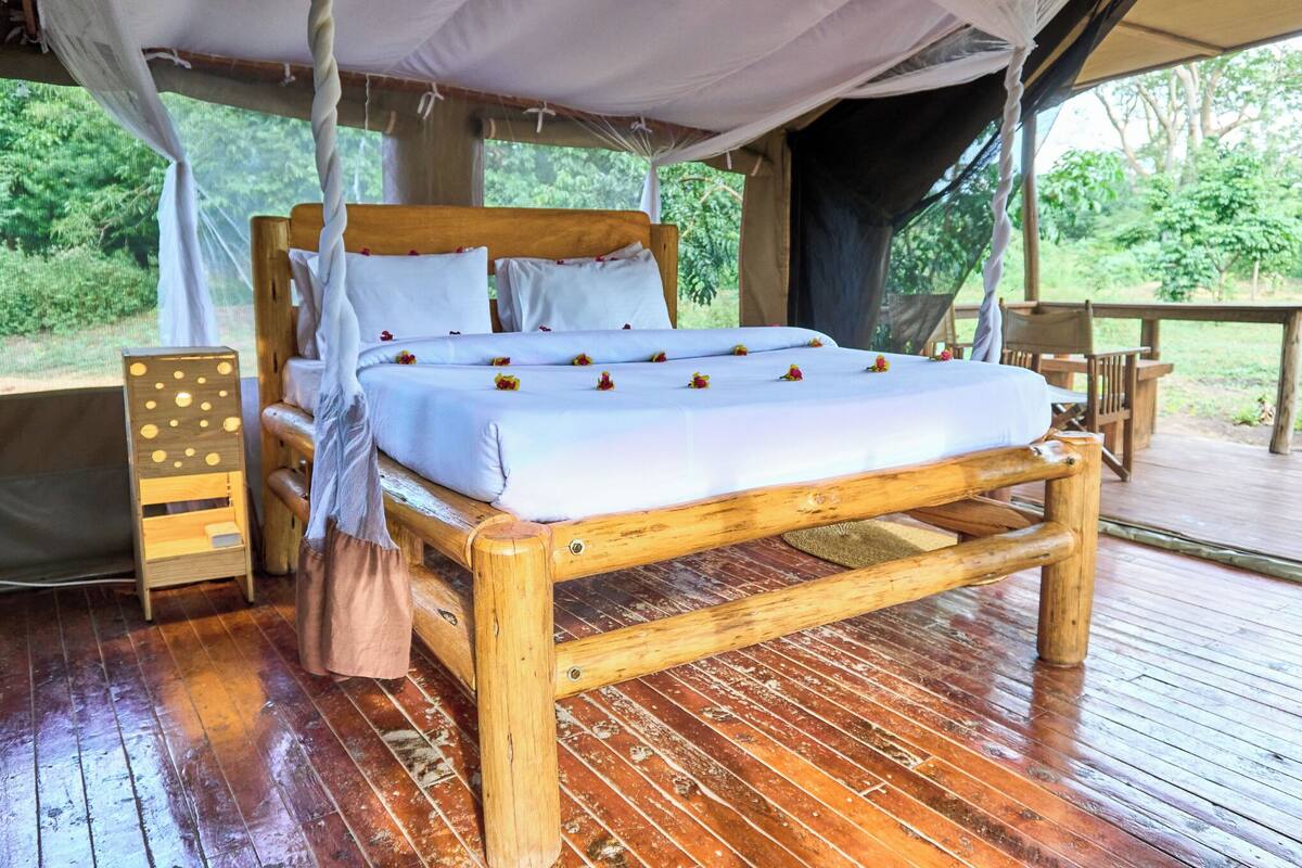 Uma cama de madeira com roupa de cama branca e um dossel, um criado-mudo de madeira e um banco.