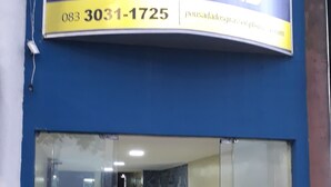 Entrada de hotel com fachada azul, uma ampla janela de vidro e área de recepção com mobiliário.