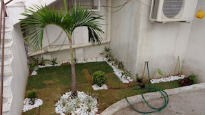 Um pequeno jardim bem cuidado, com uma palmeira, arbustos variados e pedrinhas brancas.