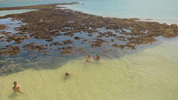Uma praia com águas claras e rasas e áreas rochosas.