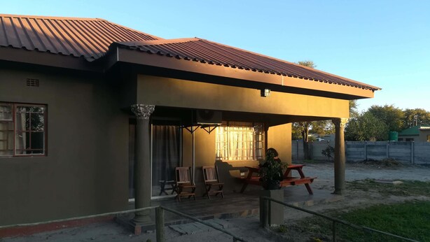 A building with a covered patio area, featuring outdoor seating and a column. - StayBridge Apartments Suites & Chalets (Maun)
