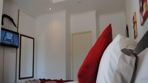 A hotel room with a bed, a television on the wall, and a door. - StayBridge Apartments Suites & Chalets (Maun)