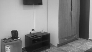 A room with a flat-screen TV mounted on the wall, a small refrigerator, a coffee maker, a cabinet, and a tiled floor. - StayBridge Apartments Suites & Chalets (Maun)