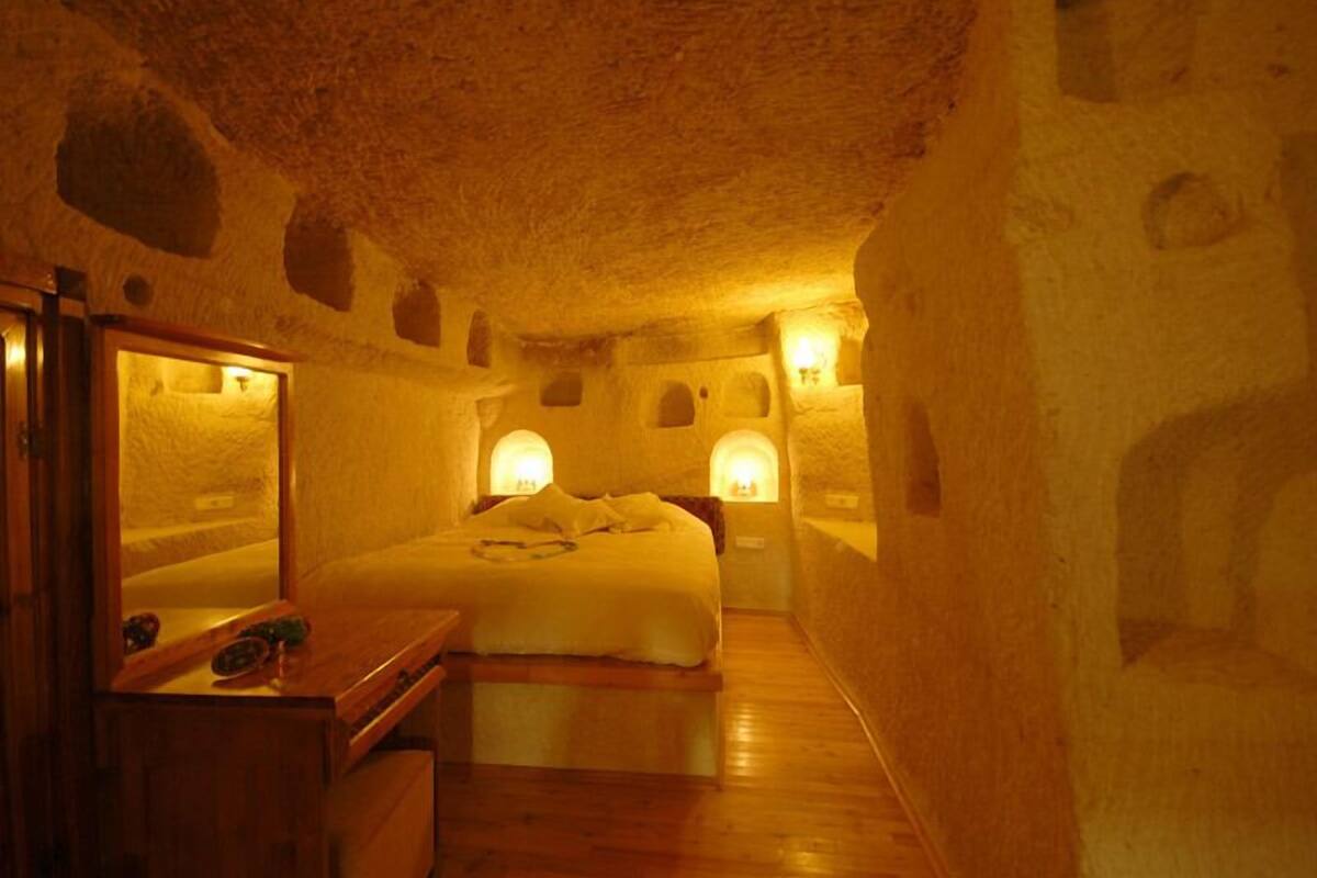 A stone-walled room with a bed, a wooden dresser, and wall-mounted lights.