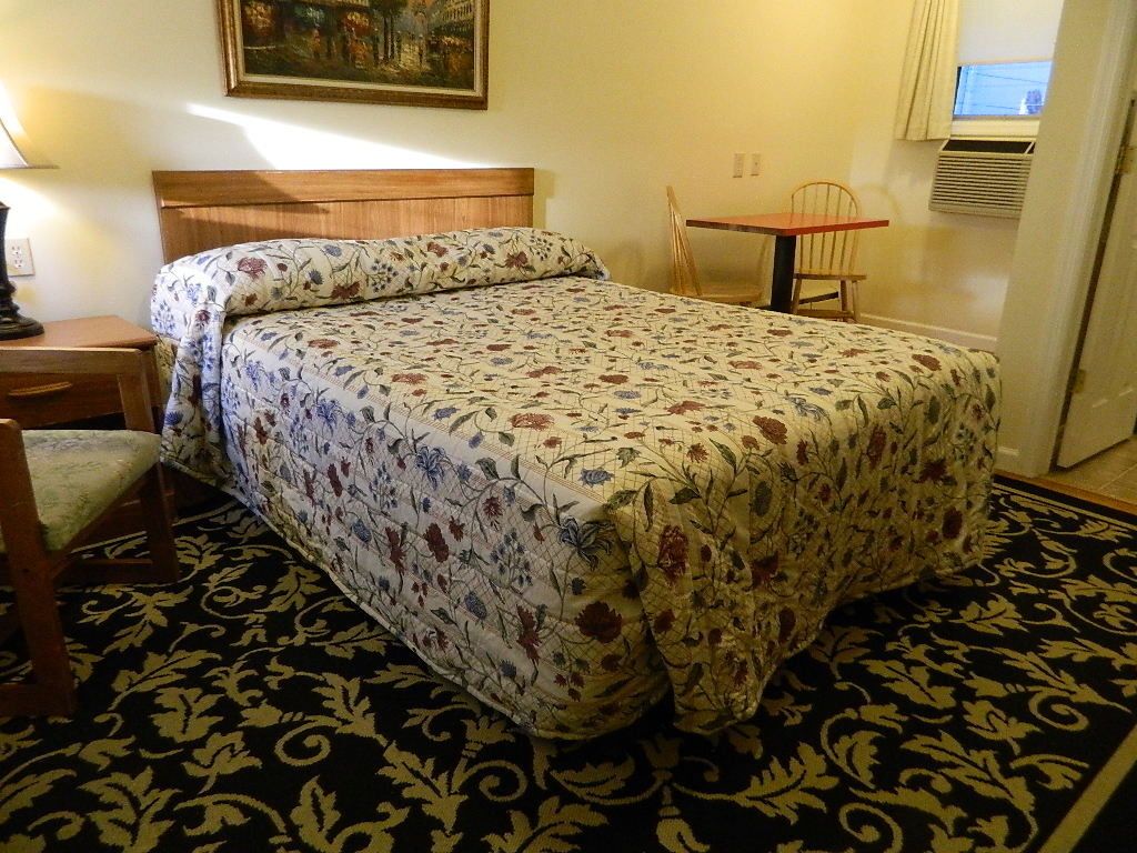 A room with a bed, a chair, a table, and a painting on the wall.