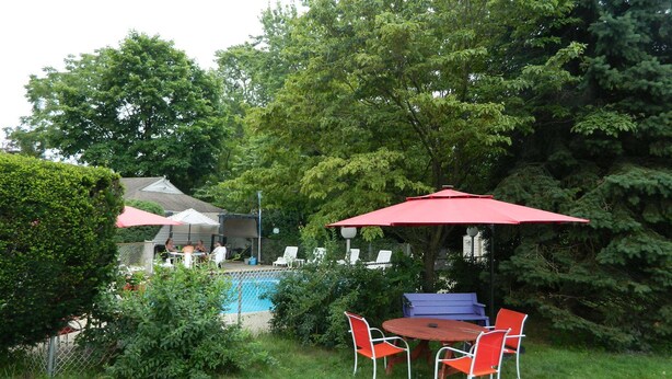 A backyard with a swimming pool, red umbrellas, and outdoor seating. - Twin Oaks Motel (Manasquan)