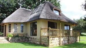 A thatched-roof house with a stone foundation, large windows, and a wooden balcony. - Imla Guest Farm (Setsoto)