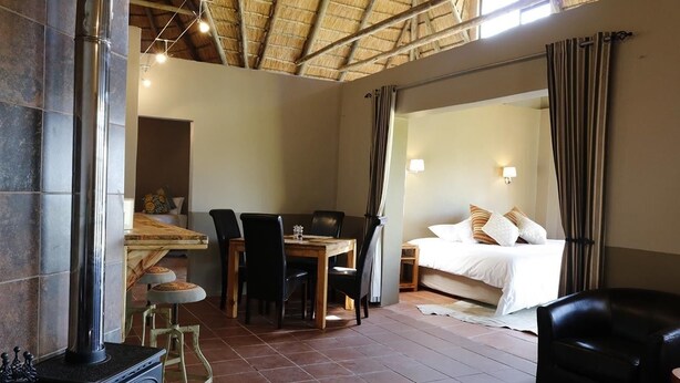 A room with a fireplace, a dining area, a bed, and a bathroom. - Imla Guest Farm (Setsoto)