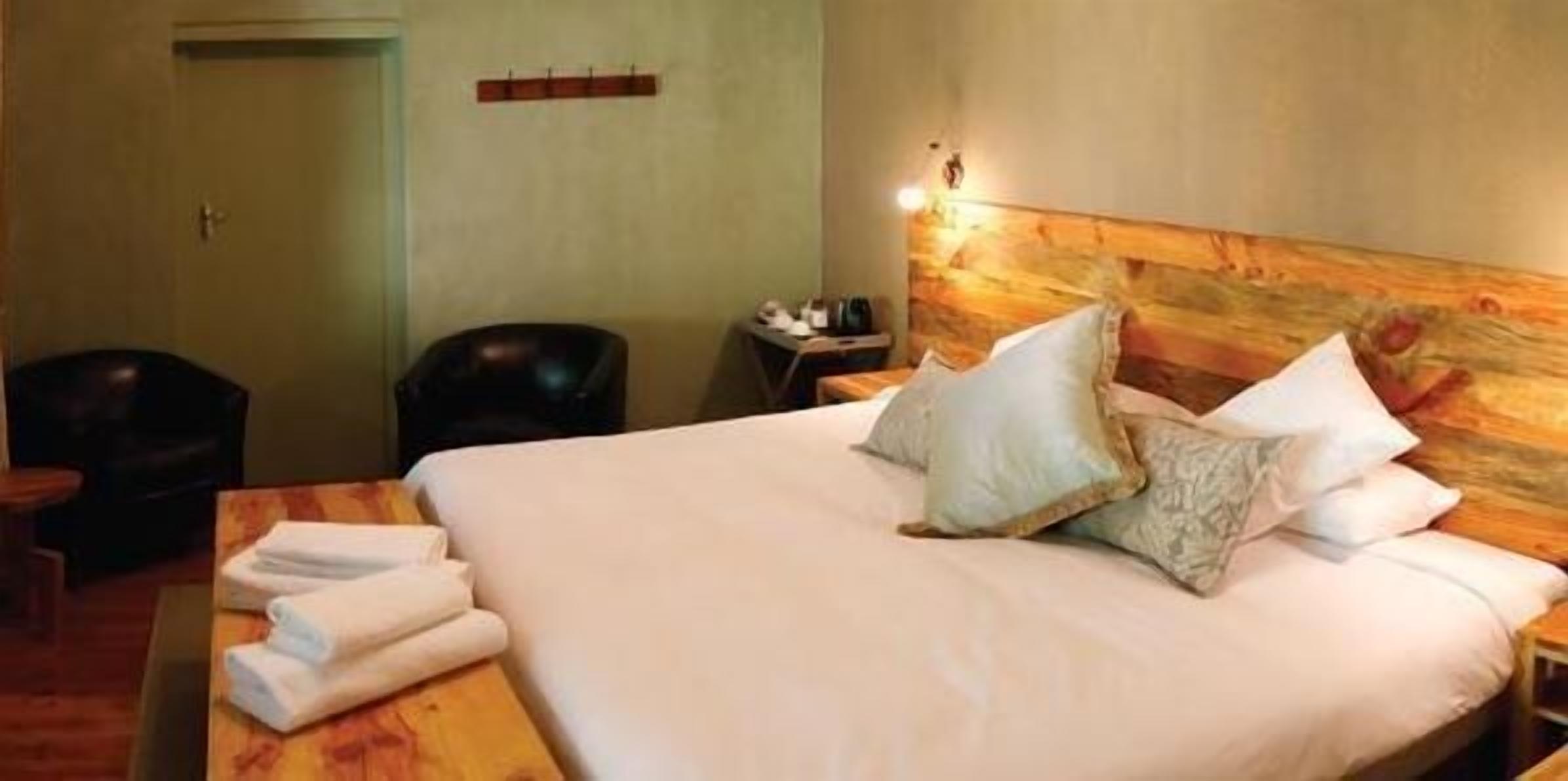 Une chambre d’hôtel avec un grand lit, une tête de lit en bois, une table de chevet avec une lampe, une chaise et une porte.