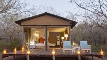 Relax in a serene bushland setting with a comfortable bed, seating area, and ambient deck lighting.
