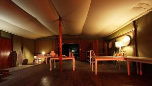 A dimly lit room with wooden floors, a table with bottles, and a lamp on a side table. - Ngama Tented Safari Lodge (Hoedspruit)