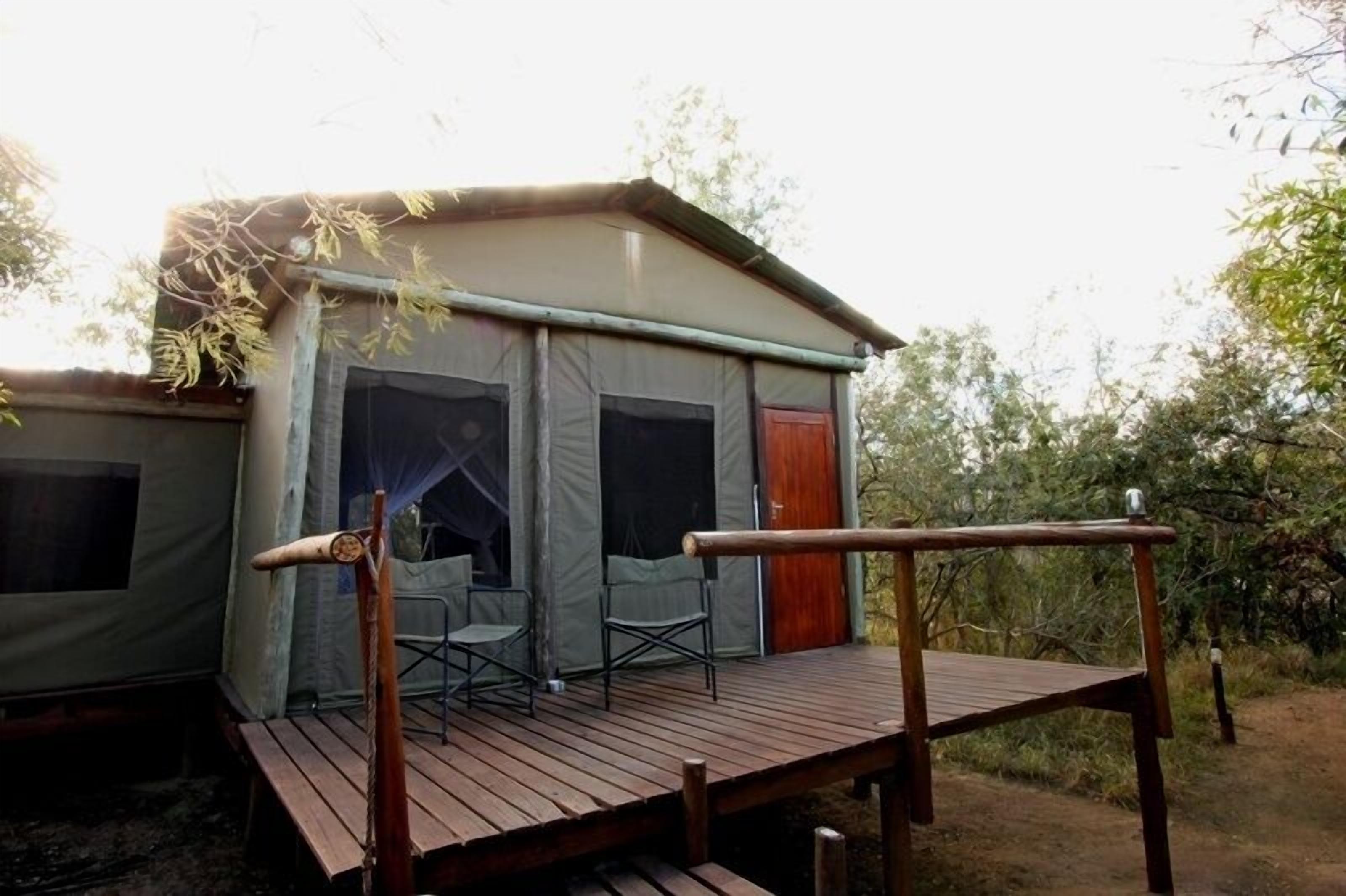 A small, single-room tent with a wooden deck and a chair.