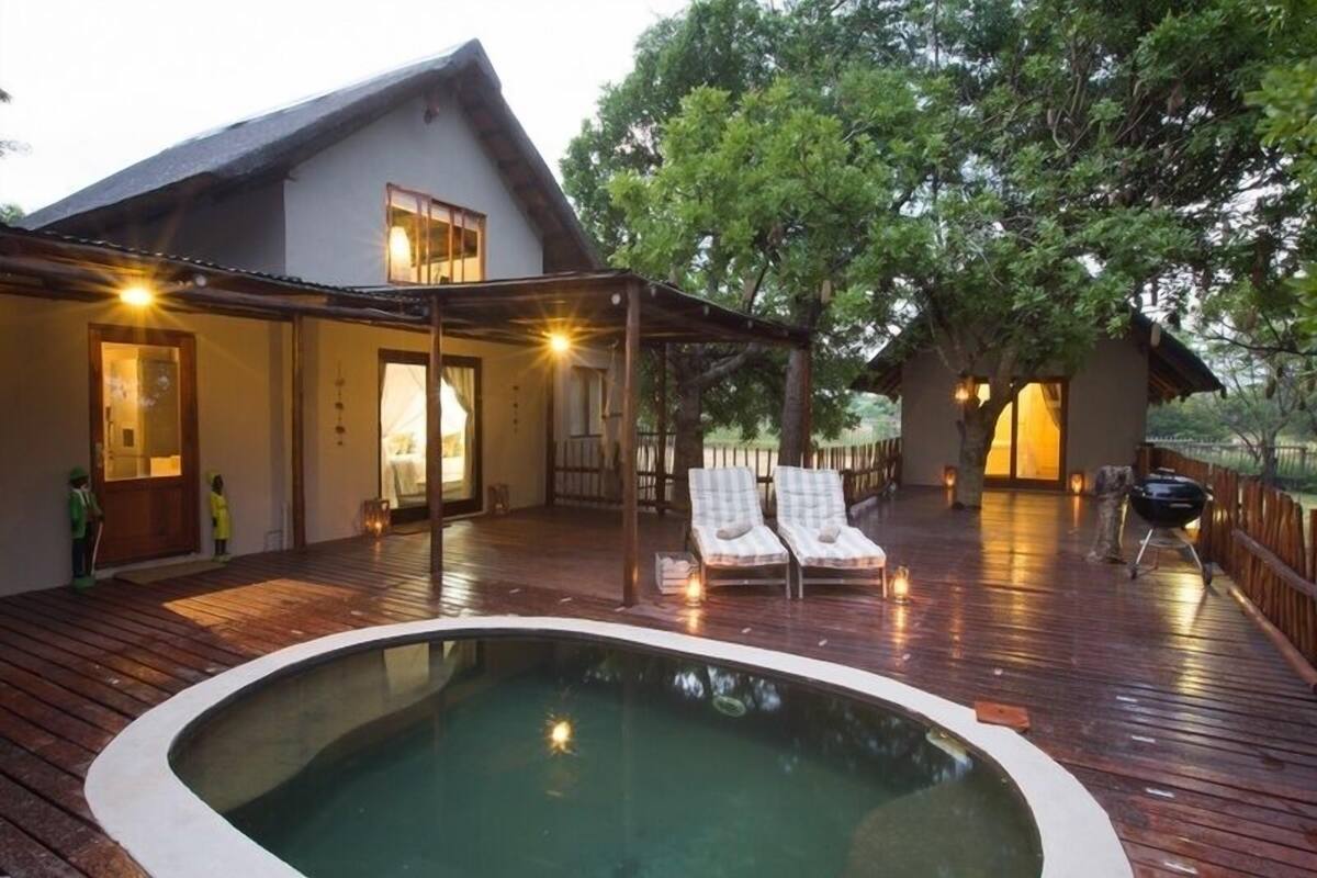 A wooden deck with a hot tub, lounge chairs, and a covered seating area.
