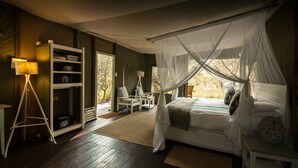 A bedroom with a canopy bed, a bedside table, a floor lamp, a chair, and a bookshelf. - Ngama Tented Safari Lodge (Hoedspruit)