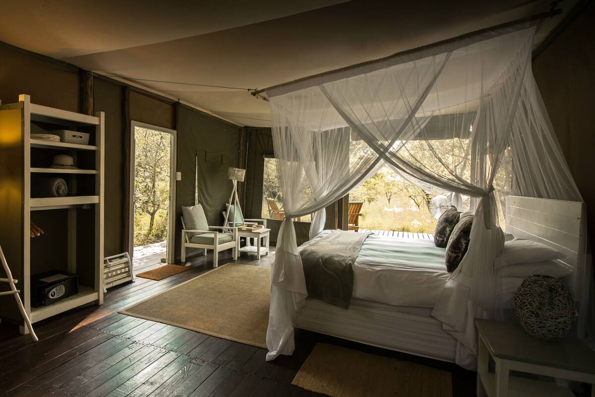 A bedroom with a canopy bed, a bedside table, a floor lamp, a chair, and a bookshelf.