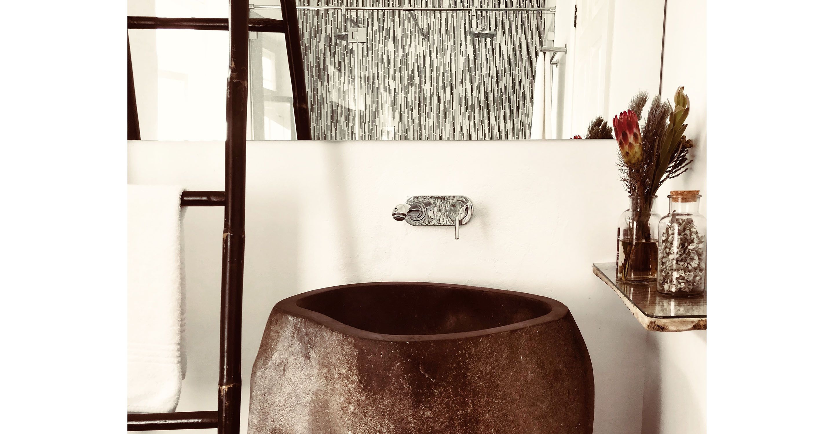 Une salle de bain dotée d’un grand lavabo rustique, d’un miroir moderne et d’une étagère ornée d’objets décoratifs.