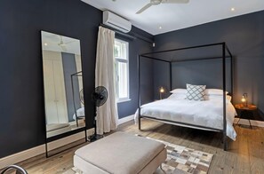 A bedroom with a four-poster bed, a large mirror, a ceiling fan, and a bedside table with a lamp.