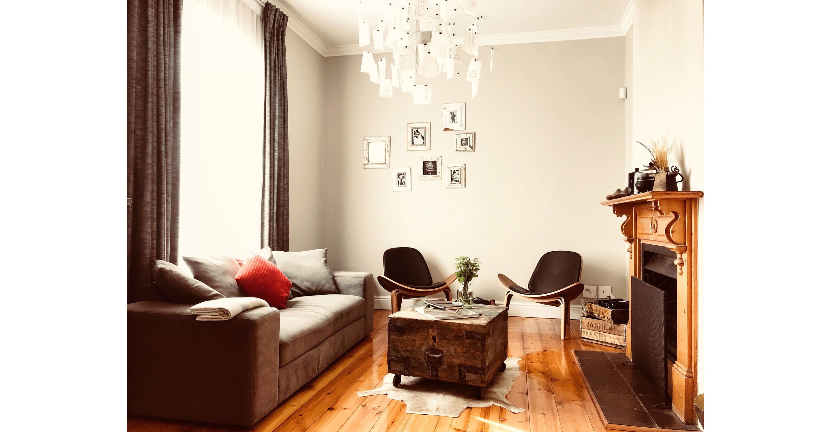 Un salon comprenant un canapé, deux fauteuils, une table basse, une cheminée et des tableaux accrochés au mur.