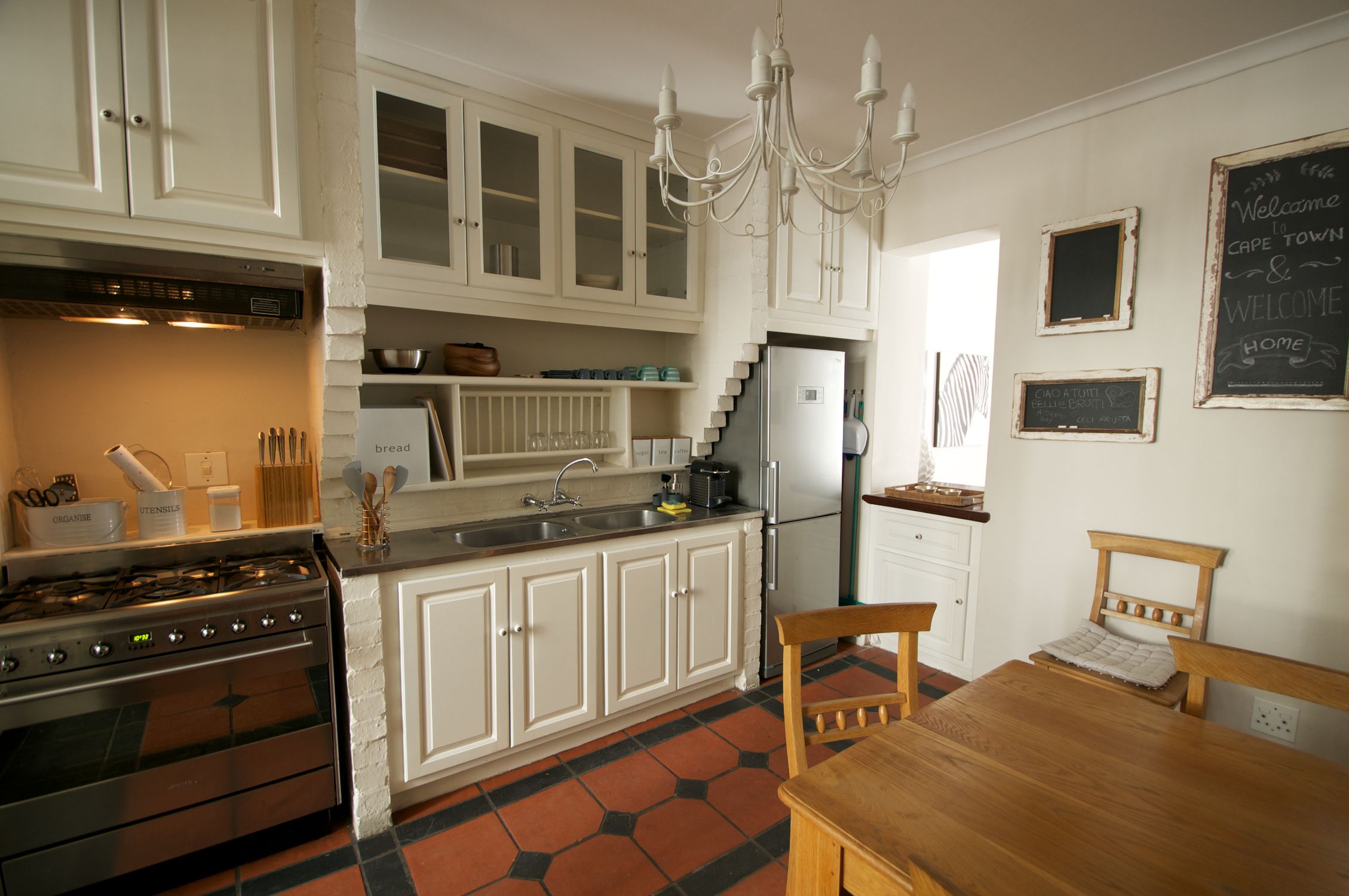 Een keuken met witte kasten, een roestvrijstalen fornuis, een koelkast en een houten eettafel.