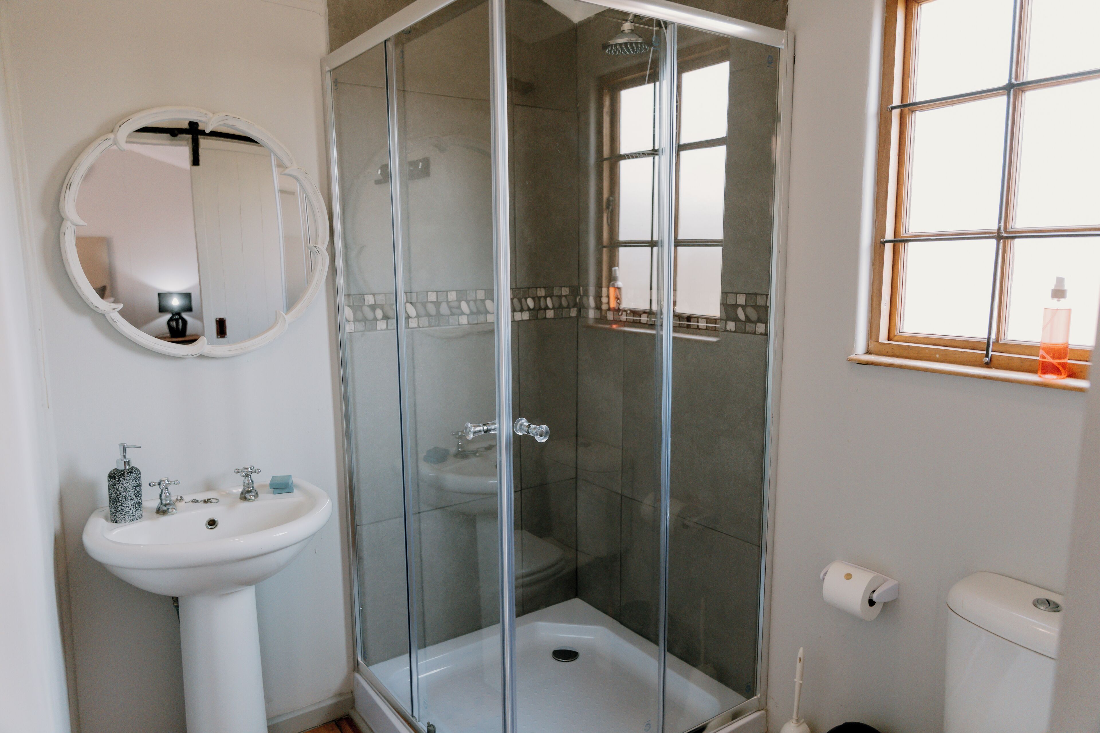 A bathroom with a glass-enclosed shower, a pedestal sink, a toilet, and a window.