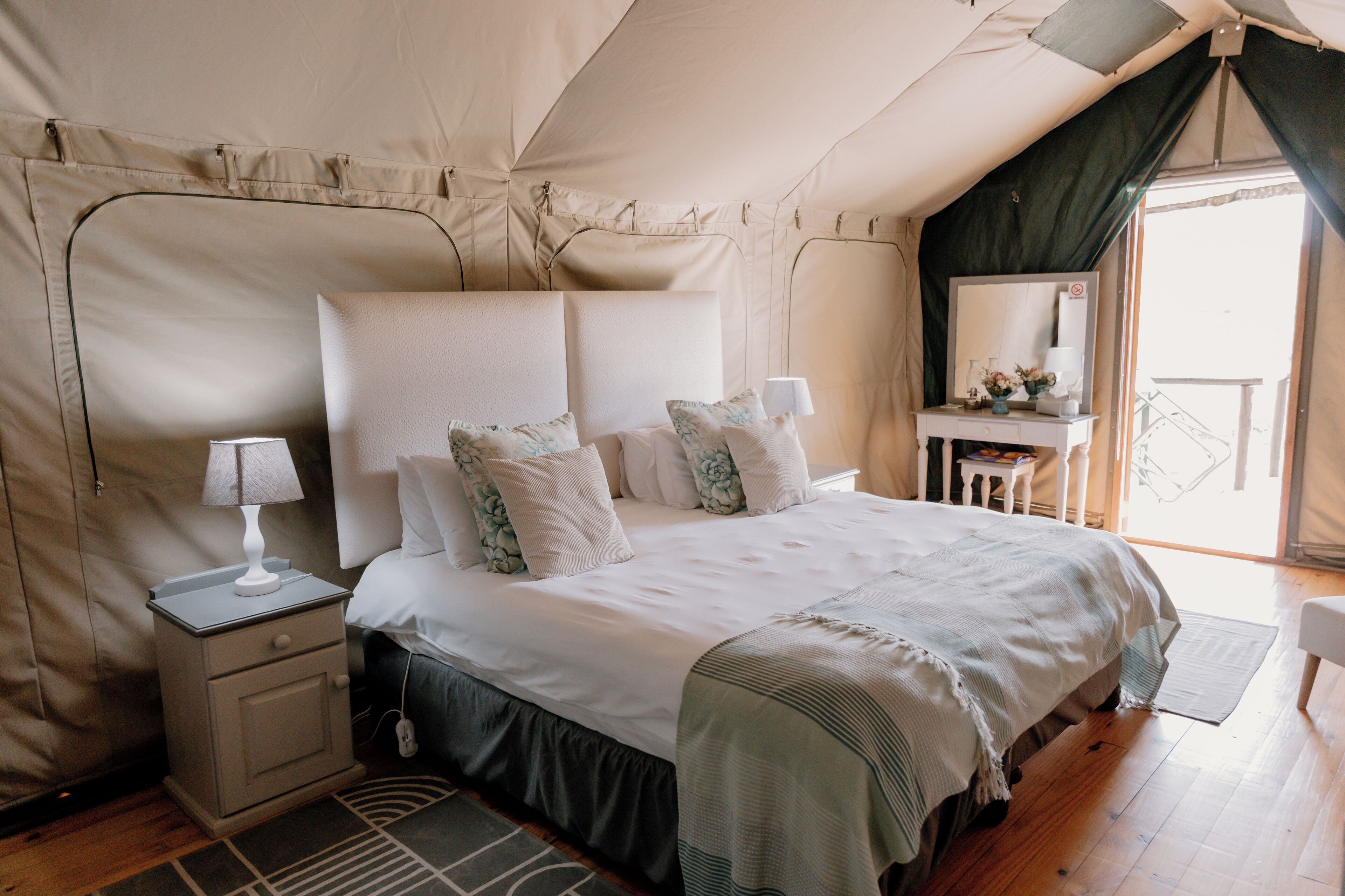 A tent-style bedroom with a bed, bedside tables, and a small desk with a mirror.