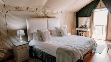 A tent-style bedroom with a bed, bedside tables, and a small desk with a mirror.