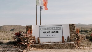 Une enseigne indiquant « Chandelier Game Lodge », avec un paysage désertique en arrière-plan.