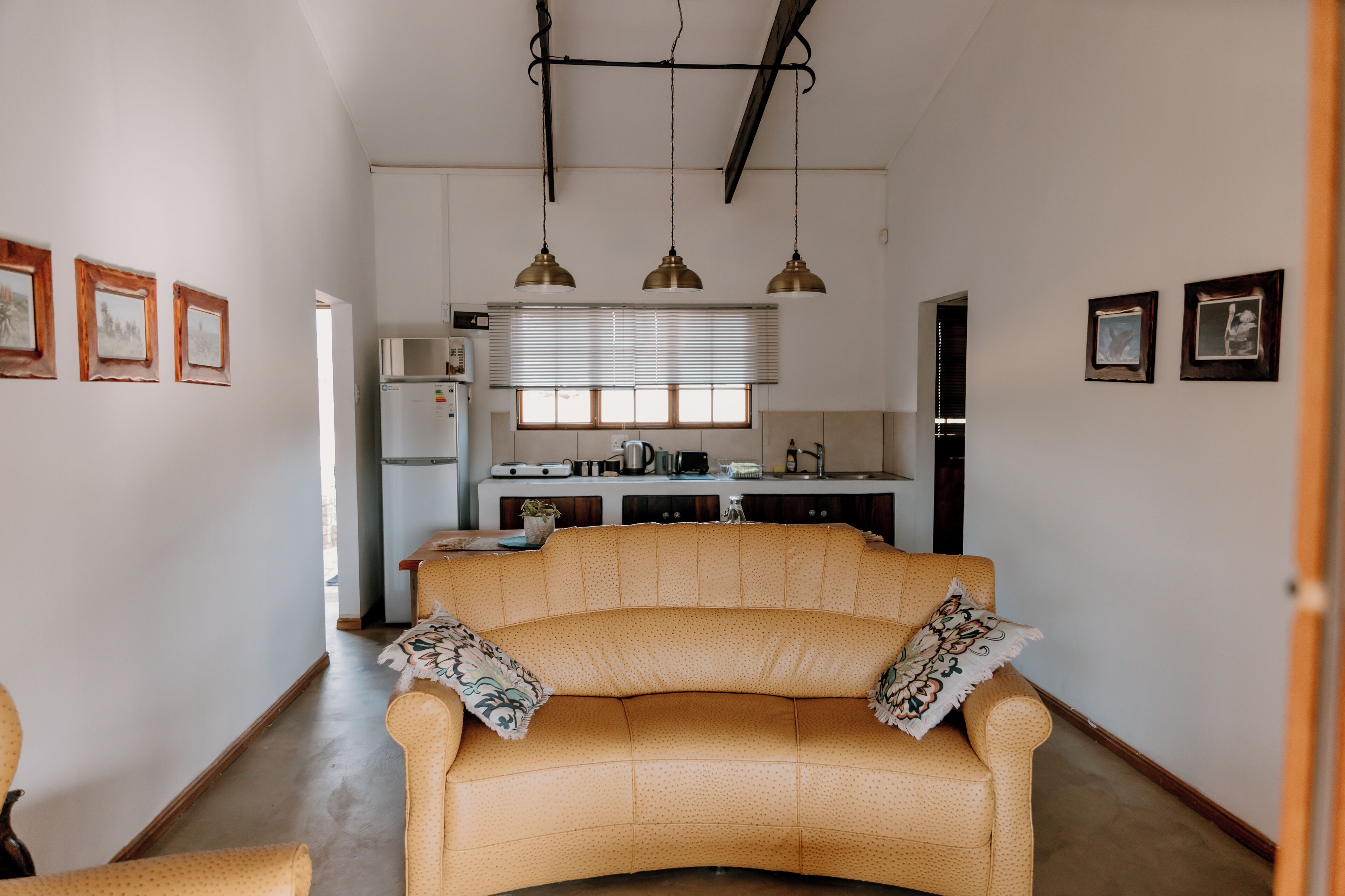 A living room with a sofa, a kitchen in the background, and framed pictures on the walls.