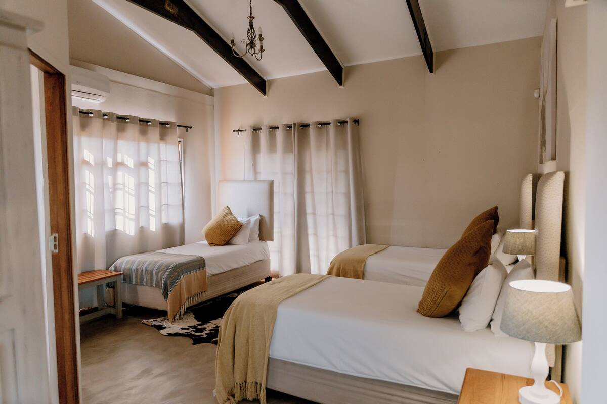 Un dormitorio con dos camas, un banco de madera, una lámpara y un ventilador de techo.