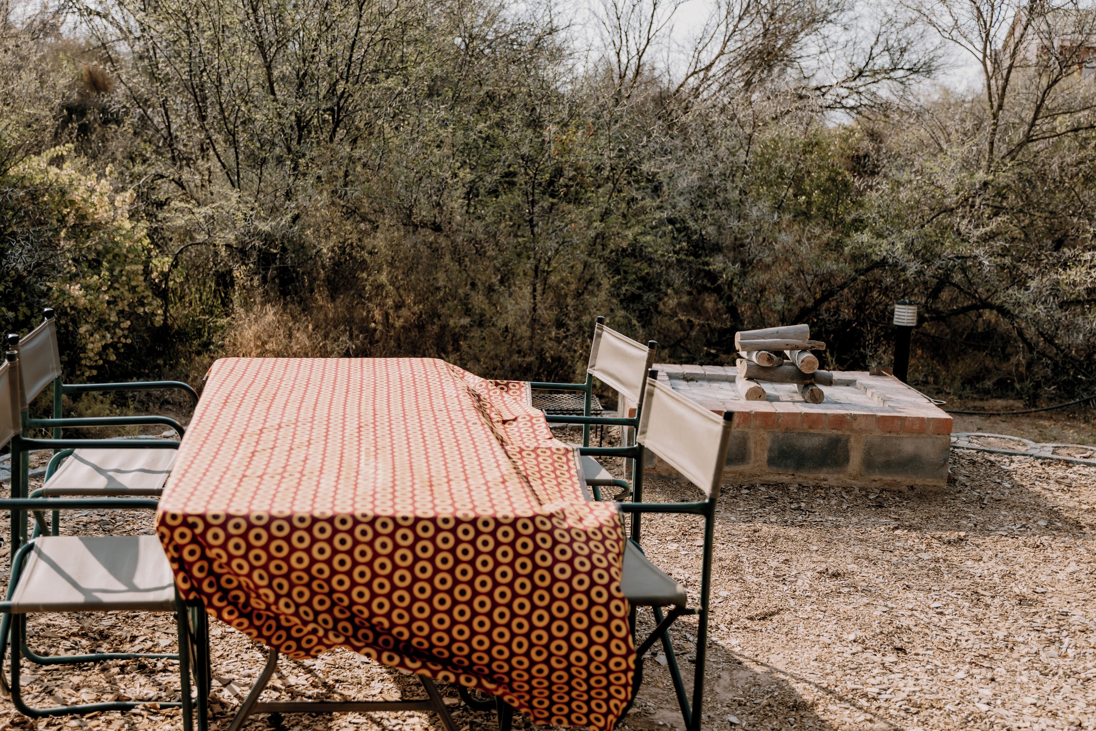 An outdoor dining area with a table covered by a patterned tablecloth, surrounded by metal chairs.