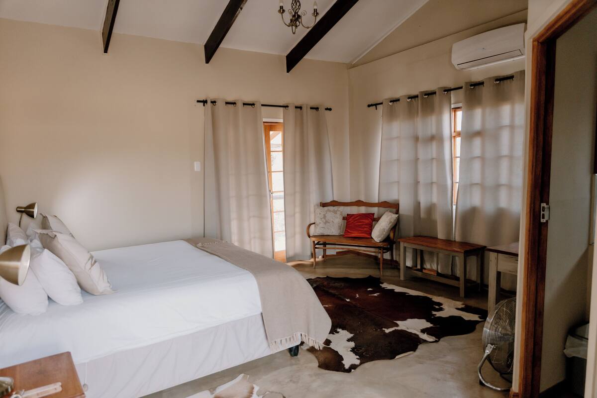 Un dormitorio con cama, un banco de madera, un tapete de cuero de vaca y un ventilador de techo.