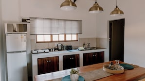 Une cuisine compacte équipée d’un réfrigérateur, d’un four à micro-ondes, d’une cuisinière et d’un évier. On y trouve des armoires en bois, une fenêtre avec des stores et une table à manger agrémentée d’un set de table et d’un vase.