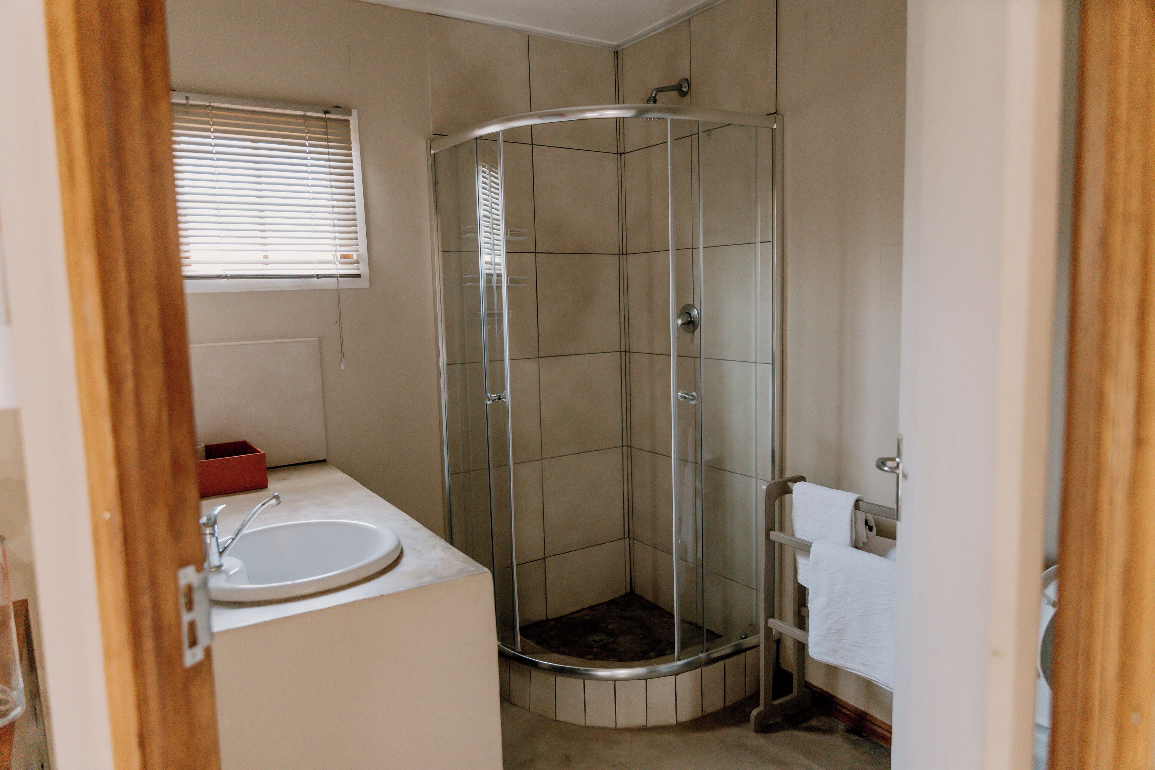 A bathroom with a glass-enclosed shower, a sink, and a window with blinds.
