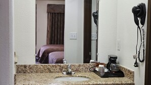 Un baño con encimera de granito, lavamanos, espejo, secador de pelo y cafetera.